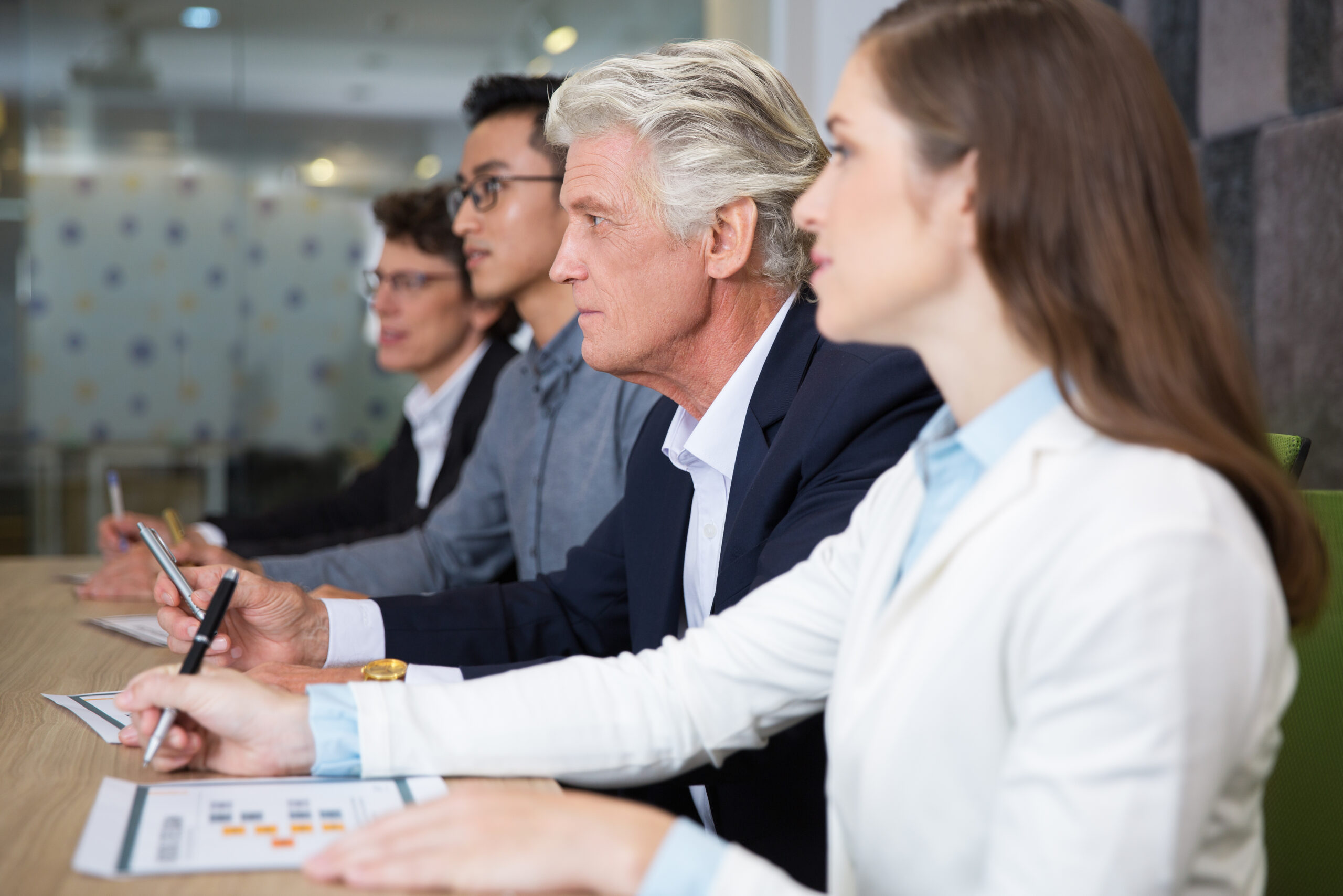 Concentrated business people attentively listening to presenter during conference. They sitting in row and looking straight. Staff making notes in papers. Audience or business meeting concept