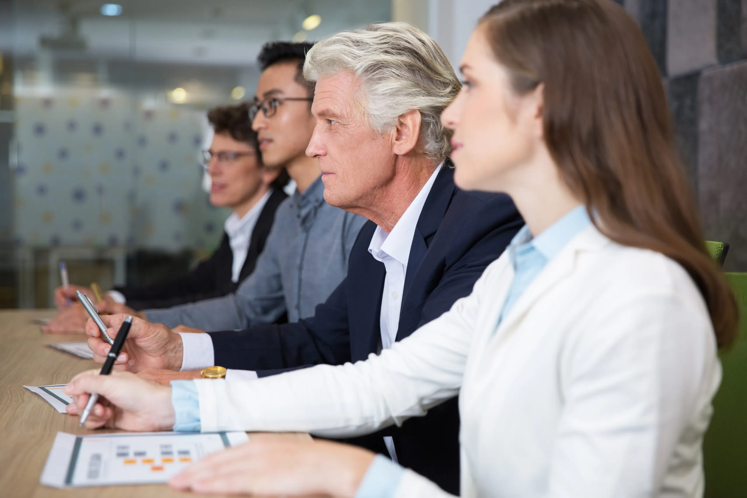 Concentrated business people attentively listening to presenter during conference. They sitting in row and looking straight. Staff making notes in papers. Audience or business meeting concept