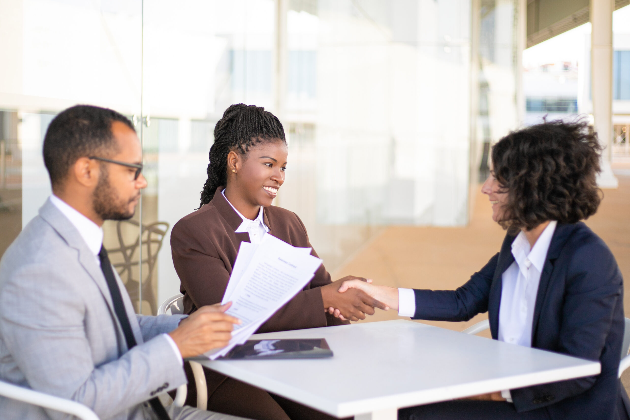 Business colleagues consulting legal advisor. Business man and women sitting at table outdoors and talking, man holding papers, women shaking hands. Consulting expert concept
