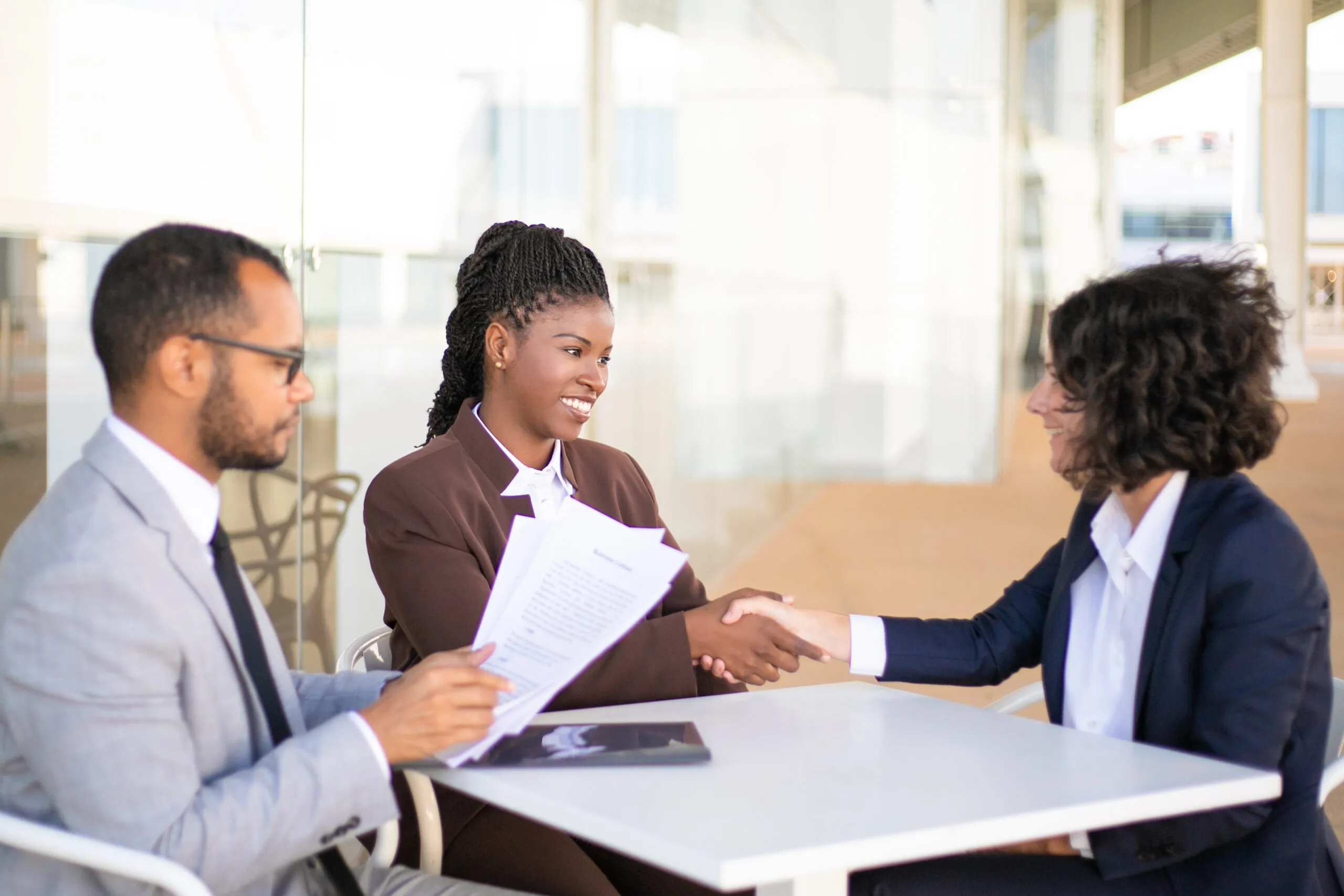 Business colleagues consulting legal advisor. Business man and women sitting at table outdoors and talking, man holding papers, women shaking hands. Consulting expert concept