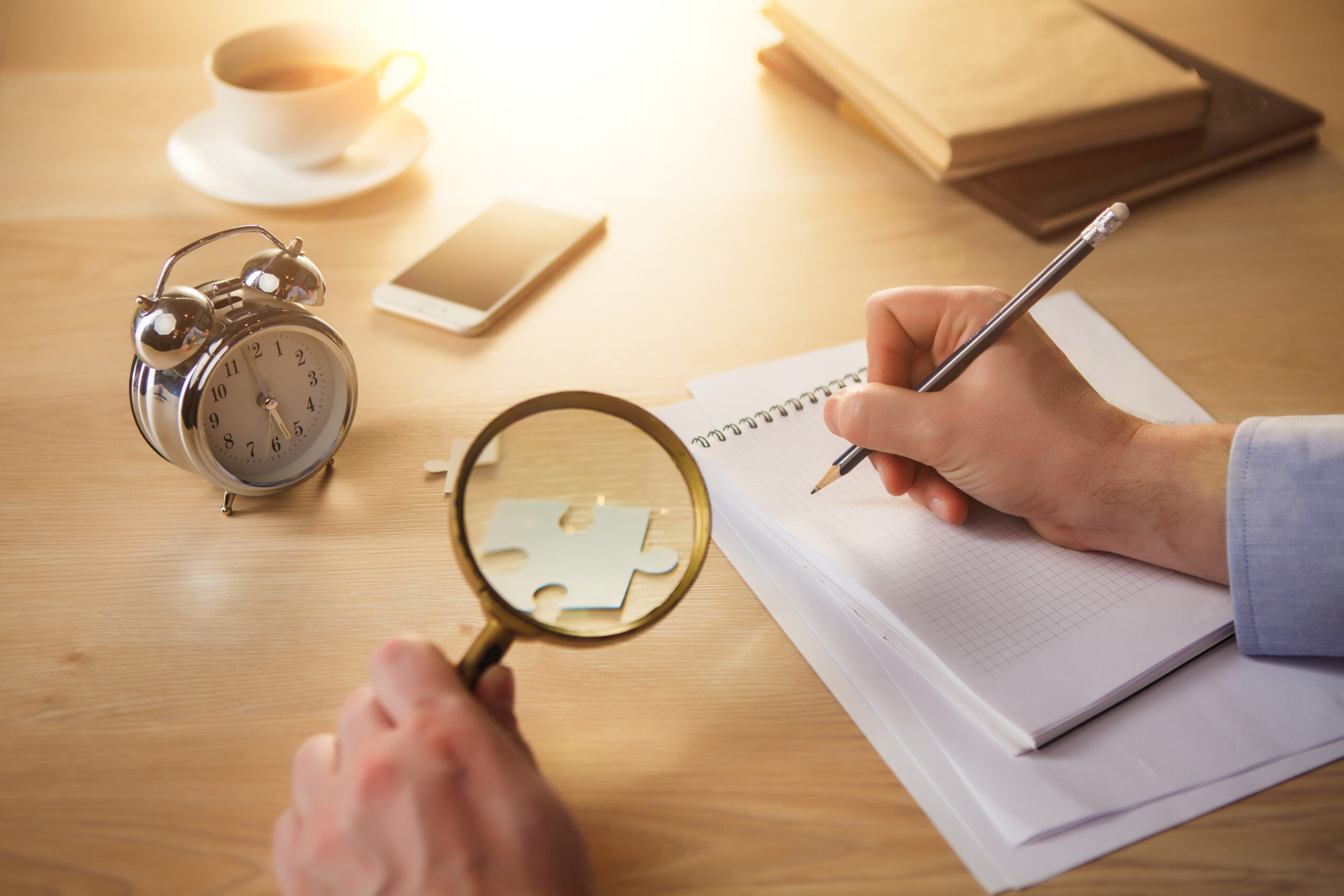 The male hands with a pencil and magnifying glass and the service hours and notebook on the table